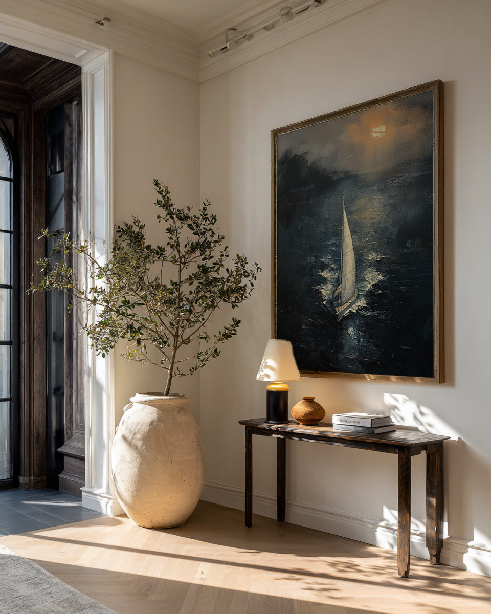 Framed sailboat painting displayed in a bright entryway above a wooden console table with a large ceramic vase.