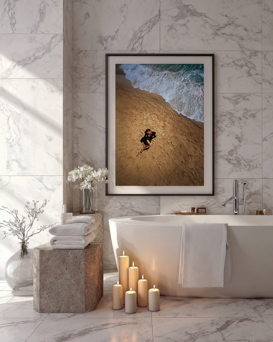 Bathroom with marble walls, bathtub, candles, and a framed picture of a person on sand.