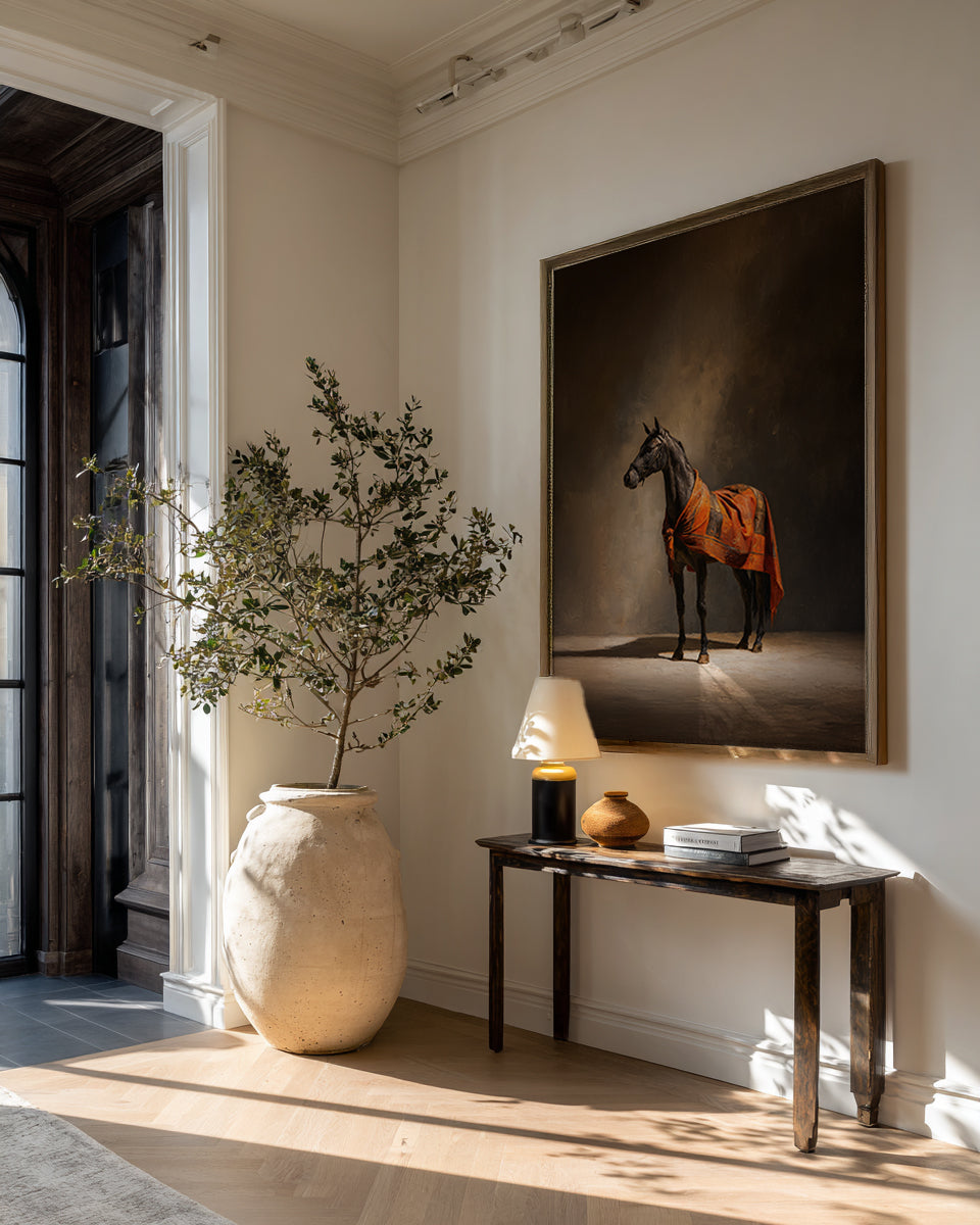 Room interior with a horse painting on the wall, a vase with plants, and a small table.