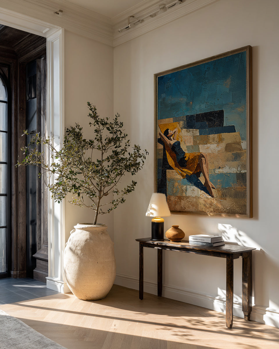 Decorative interior with a large vase, plant, and artwork on a wall.