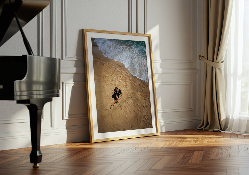 Framed artwork of a person running on a hill next to a grand piano in a room with white walls and wooden floor.